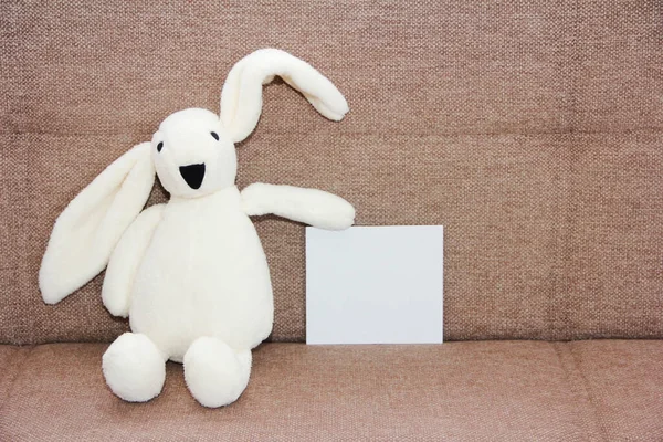 Children\'s toy white fluffy plush bunny holding a greeting card on a brown background