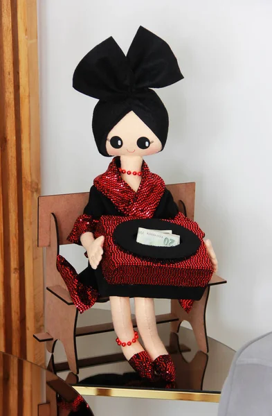 A handmade doll, the mistress of the house, in a red dress, holds a box with money