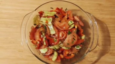 Taze sebzeler, domatesler, salatalıklar, biberler ve maydanozdan oluşan şeffaf cam bir tabakta, ahşap bir arka planda yaz salatası.