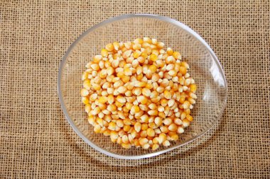 Kahverengi arka planda dekoratif bir tabakta küçük sarı mısır taneleri.