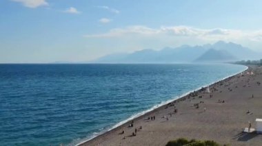 Mavi Akdeniz 'de dalgalar ve insanların yürüdüğü bir çakıl taşı plajı.
