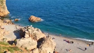 Mavi Akdeniz 'de dalgalar ve insanların yürüdüğü bir çakıl taşı plajı.