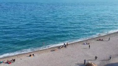 Mavi Akdeniz 'de dalgalar ve insanların yürüdüğü bir çakıl taşı plajı.