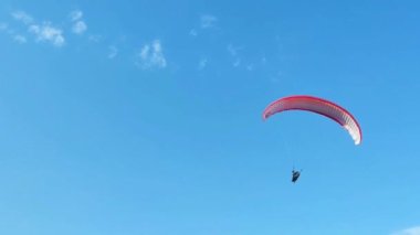 Mavi bir arka planda uçan bir adamla kırmızı bir paraglider.