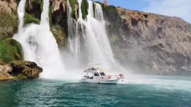 Antalya, Türkiye, 19 Mayıs 2023. Mavi Akdeniz 'de güzel bir şelalenin zemininde beyaz bir motorlu tekne yüzüyor.