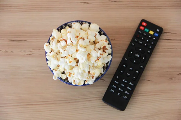 stock image White fried air popcorn in a plate and a remote control for the TV on a brown background