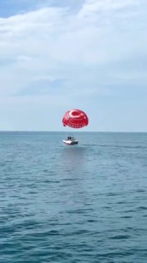 Antalya, Türkiye, 14 Mayıs 2023. Akdeniz üzerinde mavi gökyüzünde uçan bir tekneye bağlı kırmızı bir paraşüt.