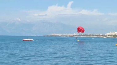 Antalya, Türkiye, 14 Mayıs 2023. Akdeniz üzerinde mavi gökyüzünde uçan bir tekneye bağlı kırmızı bir paraşüt.