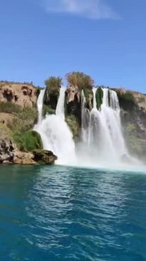 Kahverengi dağların ve mavi Akdeniz 'in arka planında büyük güzel bir şelale.