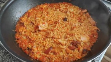 Doğal turuncu bulgur ve tavuk parçaları siyah bir tavada pişirilir.