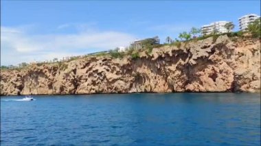 Mavi Akdeniz 'in güzel manzarası kayalık bir kıyısı ve beyaz yüzen bir teknesi var.