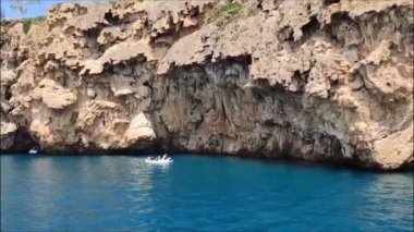 Mavi Akdeniz 'in güzel manzarası kayalık bir kıyısı ve beyaz yüzen bir teknesi var.
