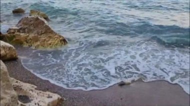 Mavi Akdeniz 'in güçlü dalgaları kumlu sahile büyük taşlarla gelir.