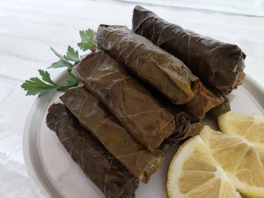 Pirinç ve etle doldurulmuş üzüm yapraklarından yapılmış geleneksel Türk dolması, maydanoz ve limon dilimleriyle dolu bir tabakta yatıyor.
