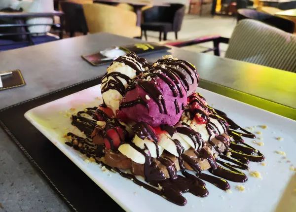 Pink and white ice cream with chocolate sauce on a baked sweet waffle on a plate on the table in a cafe