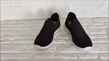 Beyaz tabanlı siyah spor ayakkabıları beyaz tuğla arka planda.