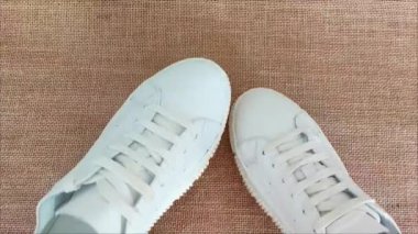 Kahverengi jüt arka planda bağcıkları olan beyaz spor deri spor ayakkabıları.