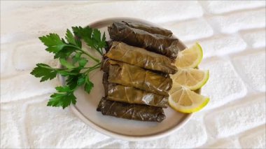 Pirinçli, maydanozlu ve limonlu, seramik tabakta üzüm yapraklarından yapılmış lezzetli bir dolma.