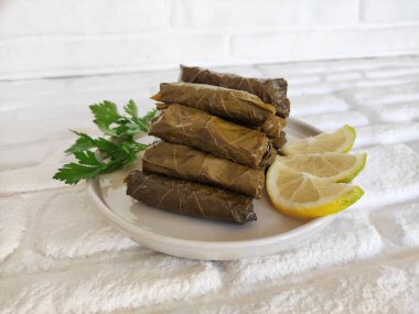 Maydanoz ve limon dilimleriyle dolu tabakta pirinçle doldurulmuş üzüm yapraklarının lezzetli domatesi.