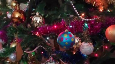 Renkli yeni yıl balonları, oyuncaklar ve yeşil bir Noel ağacının dallarında parlayan çelenkler.