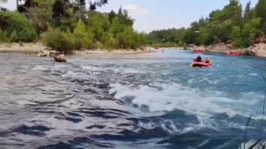 Rafting teknelerindeki insanlar nehir boyunca hızlı bir akıntıyla yol alıyorlar.