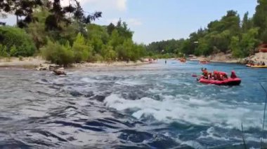 Rafting teknelerindeki insanlar nehir boyunca hızlı bir akıntıyla yol alıyorlar.