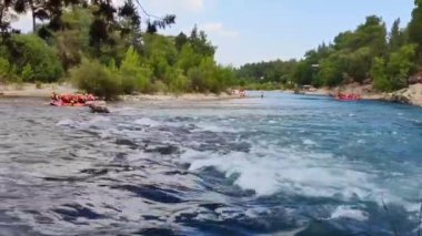 Rafting teknelerindeki insanlar nehir boyunca hızlı bir akıntıyla yol alıyorlar.