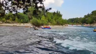 Rafting teknelerindeki insanlar nehir boyunca hızlı bir akıntıyla yol alıyorlar.