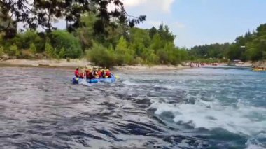 Rafting teknelerindeki insanlar nehir boyunca hızlı bir akıntıyla yol alıyorlar.