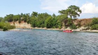 Rafting teknelerindeki yelekli insanlar hızlı bir dağ nehri boyunca yelken açıyorlar.