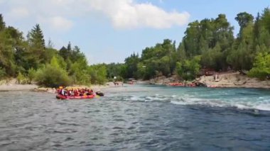 Rafting teknelerindeki yelekli insanlar hızlı bir dağ nehri boyunca yelken açıyorlar.