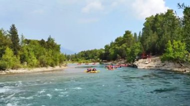 Rafting teknelerindeki yelekli insanlar hızlı bir dağ nehri boyunca yelken açıyorlar.