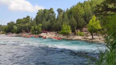 Rafting teknelerindeki yelekli insanlar hızlı bir dağ nehri boyunca yelken açıyorlar.