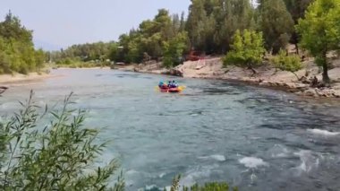 Rafting teknelerindeki yelekli insanlar hızlı bir dağ nehri boyunca yelken açıyorlar.
