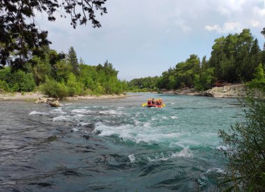 Yelek ve miğferli bir sürü insan hızlı bir dağ nehrinde rafting tekneleriyle yelken açıyor.
