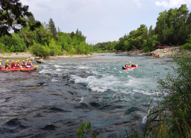 Yelek ve miğferli bir sürü insan hızlı bir dağ nehrinde rafting tekneleriyle yelken açıyor.