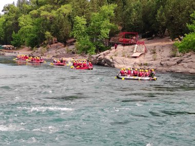 Yelek ve miğferli bir sürü insan hızlı bir dağ nehrinde rafting tekneleriyle yelken açıyor.