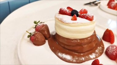 Lezzetli tatlı Japon tatlısı, yuvarlak yumurta kabarık, çikolata soslu ve çilekli krep, beyaz tabakta.