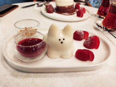  Lezzetli beyaz Japon tatlısı, kedi şeklinde puding, çilek ve meyve soslu bir tabakta.