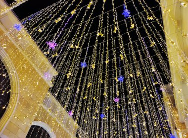 Şehrin caddesinde, karanlık gökyüzüne karşı yanan LED lambaları ve dekoratif çiçekleri olan parlak çelenkler.