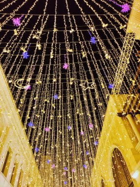 Şehrin caddesinde, karanlık gökyüzüne karşı yanan LED lambaları ve dekoratif çiçekleri olan parlak çelenkler.