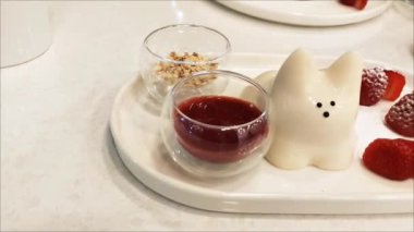 Lezzetli beyaz Japon tatlısı, kedi şeklinde puding, çilek ve meyve soslu bir tabakta.