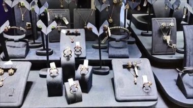Kadın mücevherleri, yüzükler, küpeler, bilezikler ve vitrinde değerli taşlar olan kolyeler.