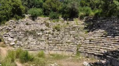 Eski şehrin eski harabe amfi tiyatrosu, taş duvarlar ve yeşil bitki örtüsüyle