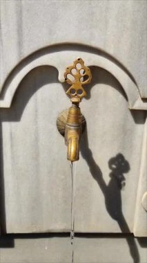 Mermer bir duvardaki dekoratif metal musluk, doğulu Osmanlı tarzında, oyma saplı ve bronz kaplamalı.