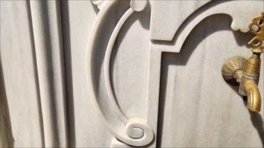 Mermer bir duvardaki dekoratif metal musluk, doğulu Osmanlı tarzında, oyma saplı ve bronz kaplamalı.