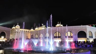  Antalya, Türkiye, 12 Haziran 2025. Meydanda parlak renkli ışıklandırması olan akşam çeşmesi. Mavi, mor, pembe ve yeşil tonlarda LED ışığıyla aydınlatılan yüksek su püskürtüleri