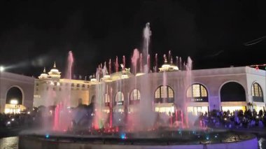  Antalya, Türkiye, 12 Haziran 2025. Meydanda parlak renkli ışıklandırması olan akşam çeşmesi. Mavi, mor, pembe ve yeşil tonlarda LED ışığıyla aydınlatılan yüksek su püskürtüleri