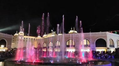  Antalya, Türkiye, 12 Haziran 2025. Meydanda parlak renkli ışıklandırması olan akşam çeşmesi. Mavi, mor, pembe ve yeşil tonlarda LED ışığıyla aydınlatılan yüksek su püskürtüleri