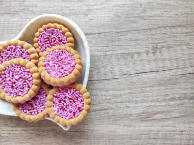 Yuvarlak pişmiş tatlı bisküviler, parlak kırmızı dolgu ve pembe pasta parçacıkları, dekoratif bir tabakta
